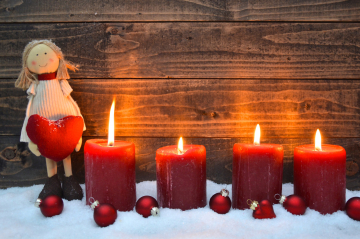 Vier rote brennende Kerzen, nebenan ein Stoffpüppchen mit einem roten Herz; im weihnachtlichen Ambiente.